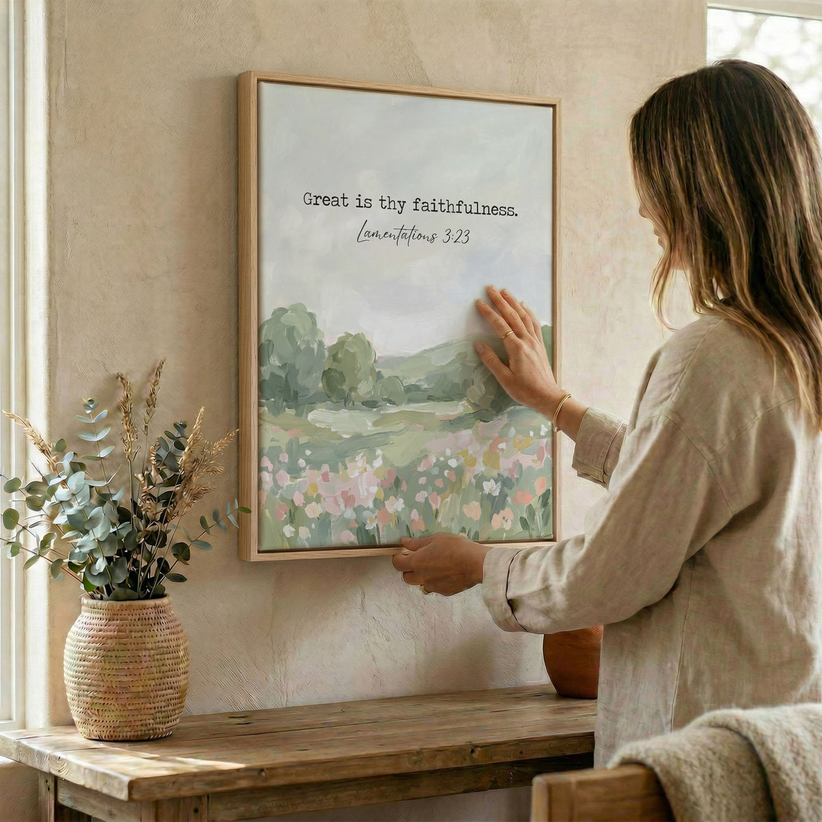 Woman hanging Bible verse wall art in wood frame beside dried botanical arrangement