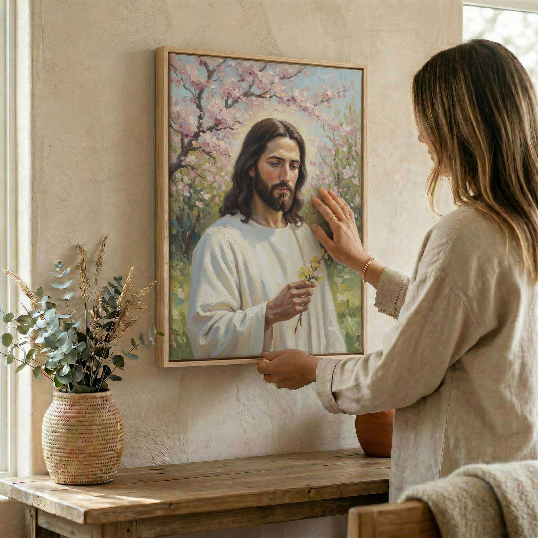 Woman hanging Jesus blossom wall art in wood frame beside dried botanical arrangement