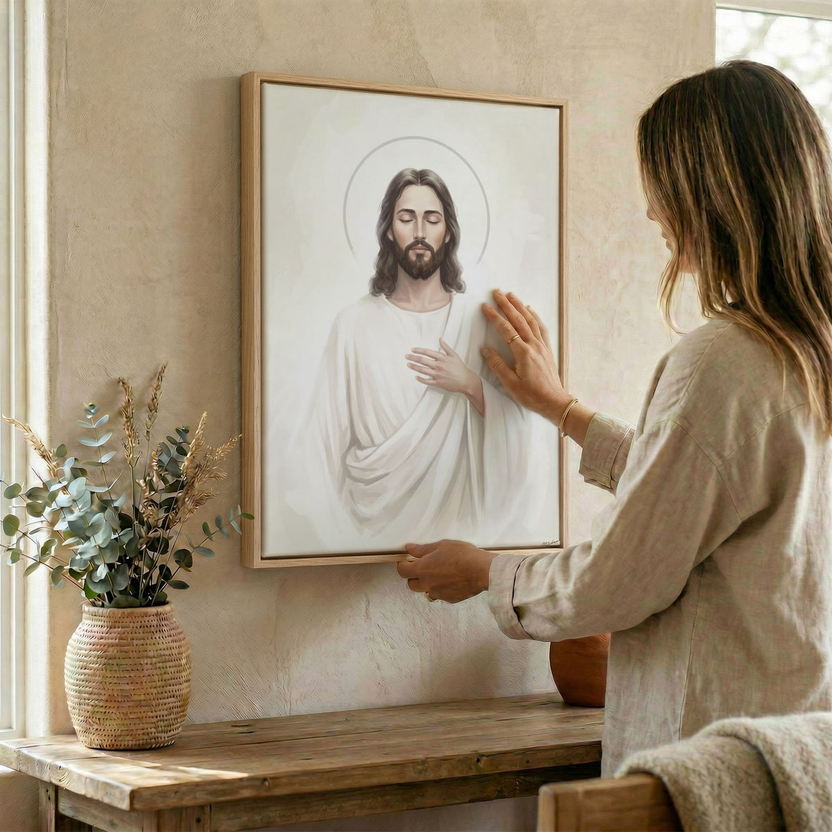 Woman hanging framed Jesus Christ portrait canvas print on textured wall above wooden console table