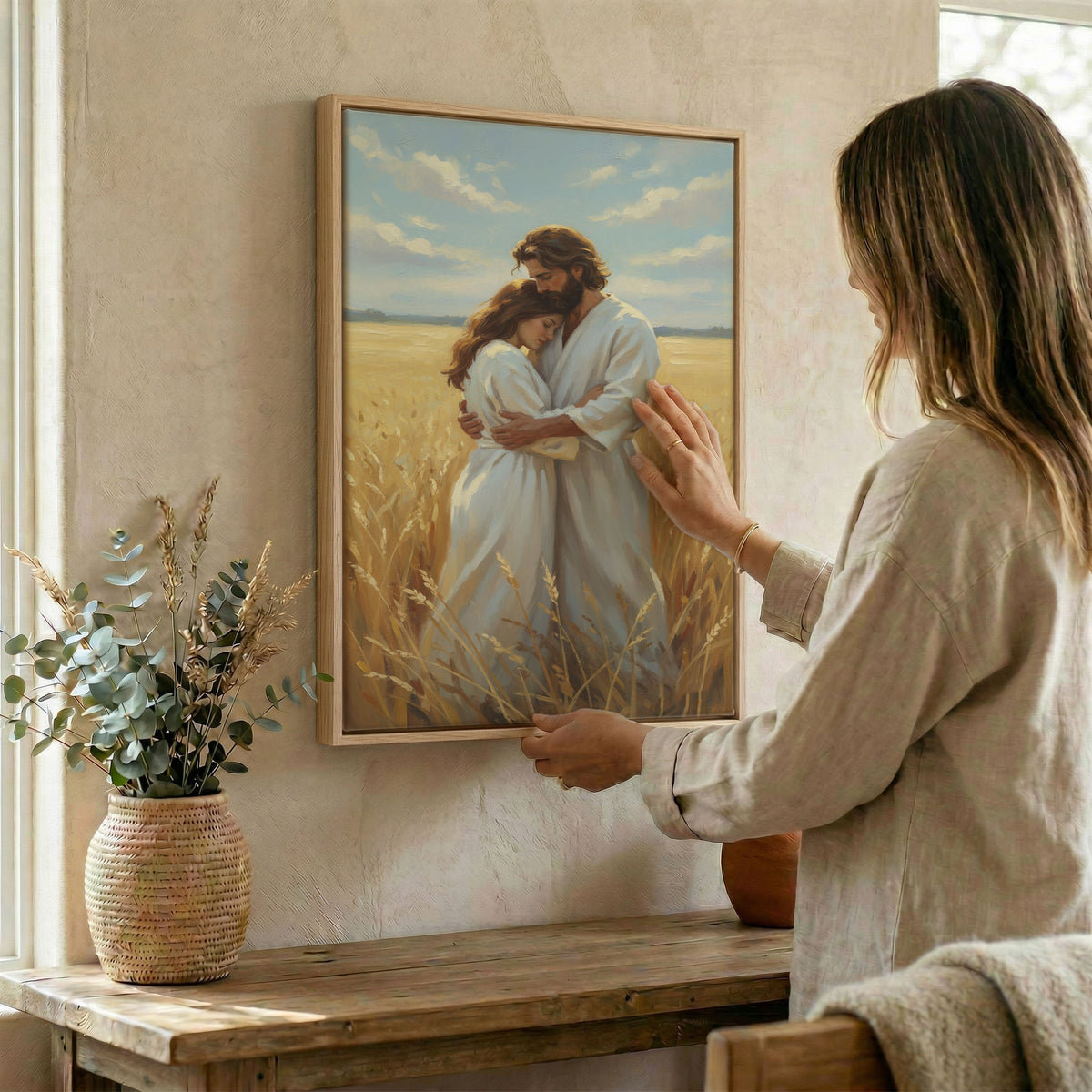 Woman hanging framed Jesus embracing woman canvas print on textured wall above wooden console
