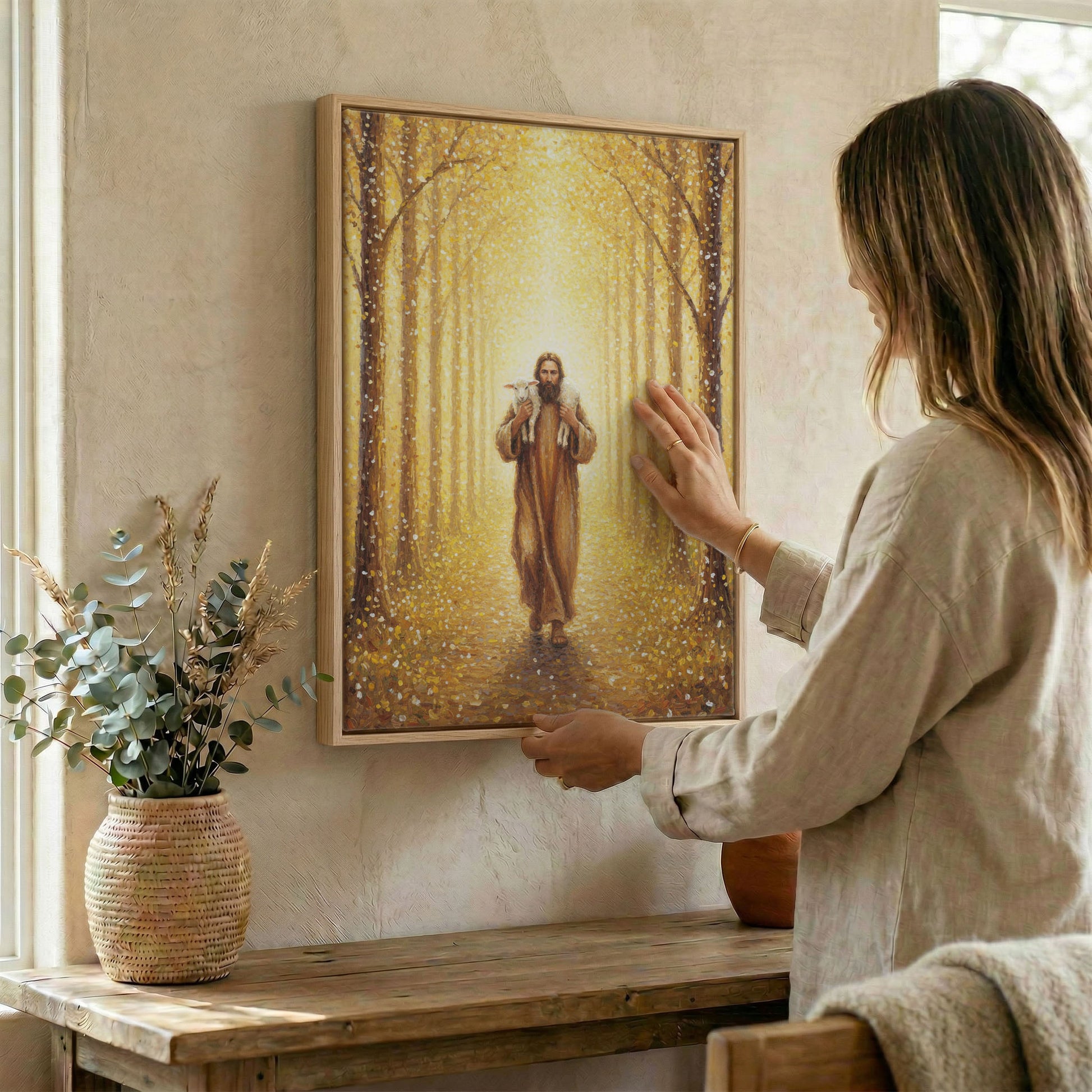 Woman hanging framed Jesus Good Shepherd canvas print on textured wall above wooden console table