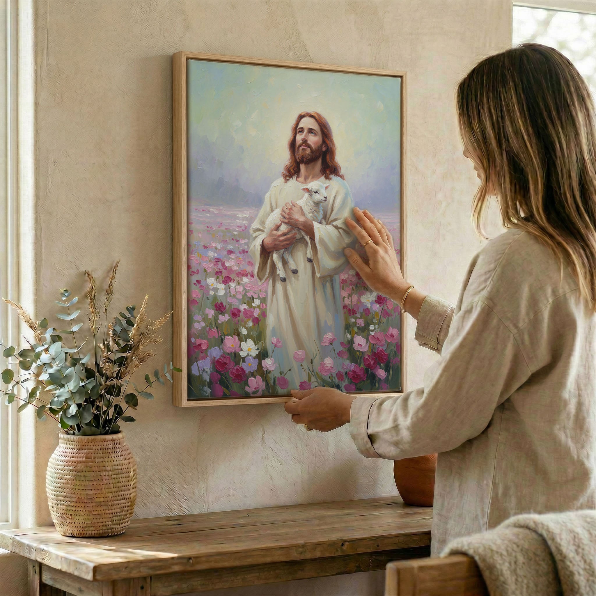 Woman hanging Jesus and lamb wall art in wood frame beside dried botanical arrangement