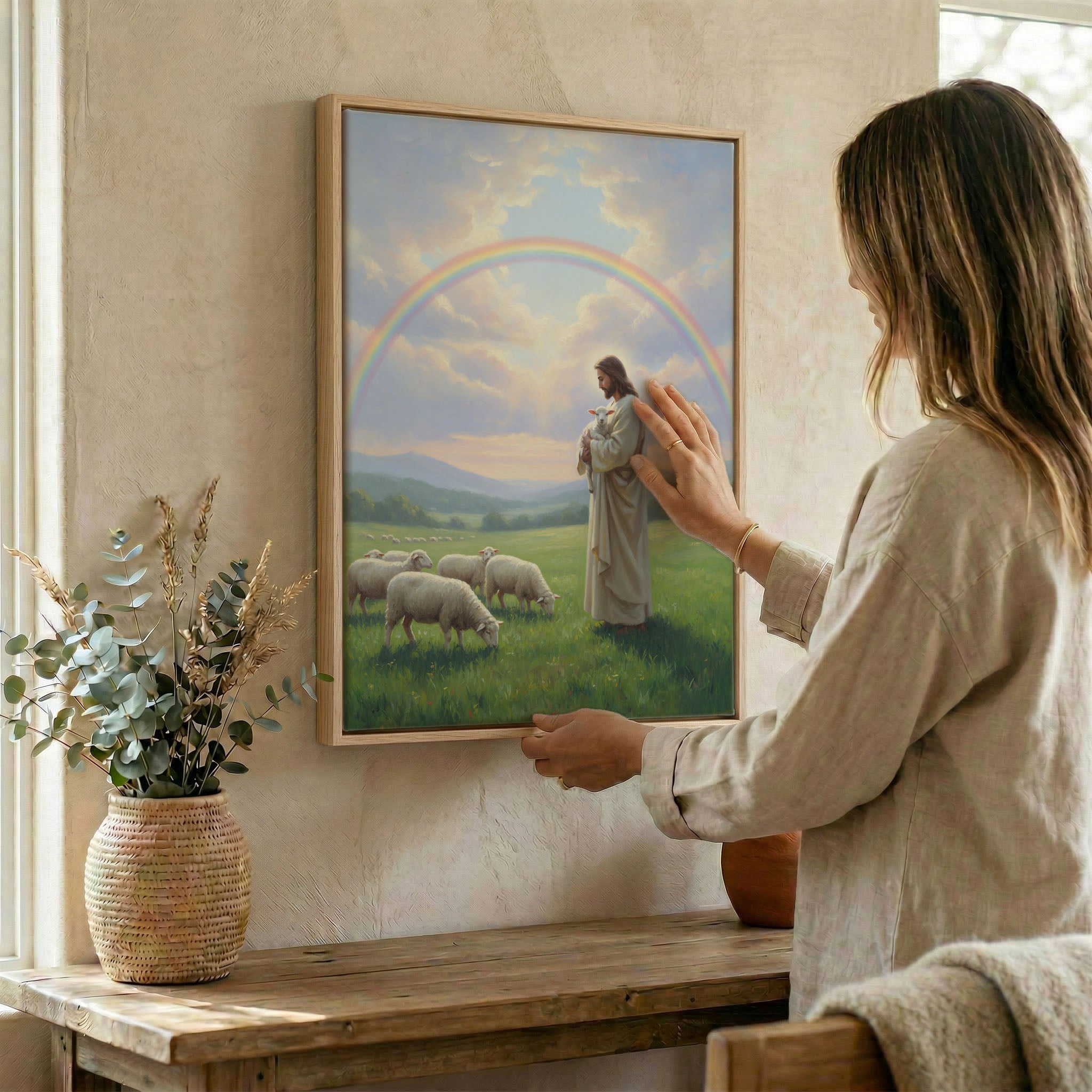 Woman hanging Jesus and lamb wall art in wood frame beside dried botanical arrangement
