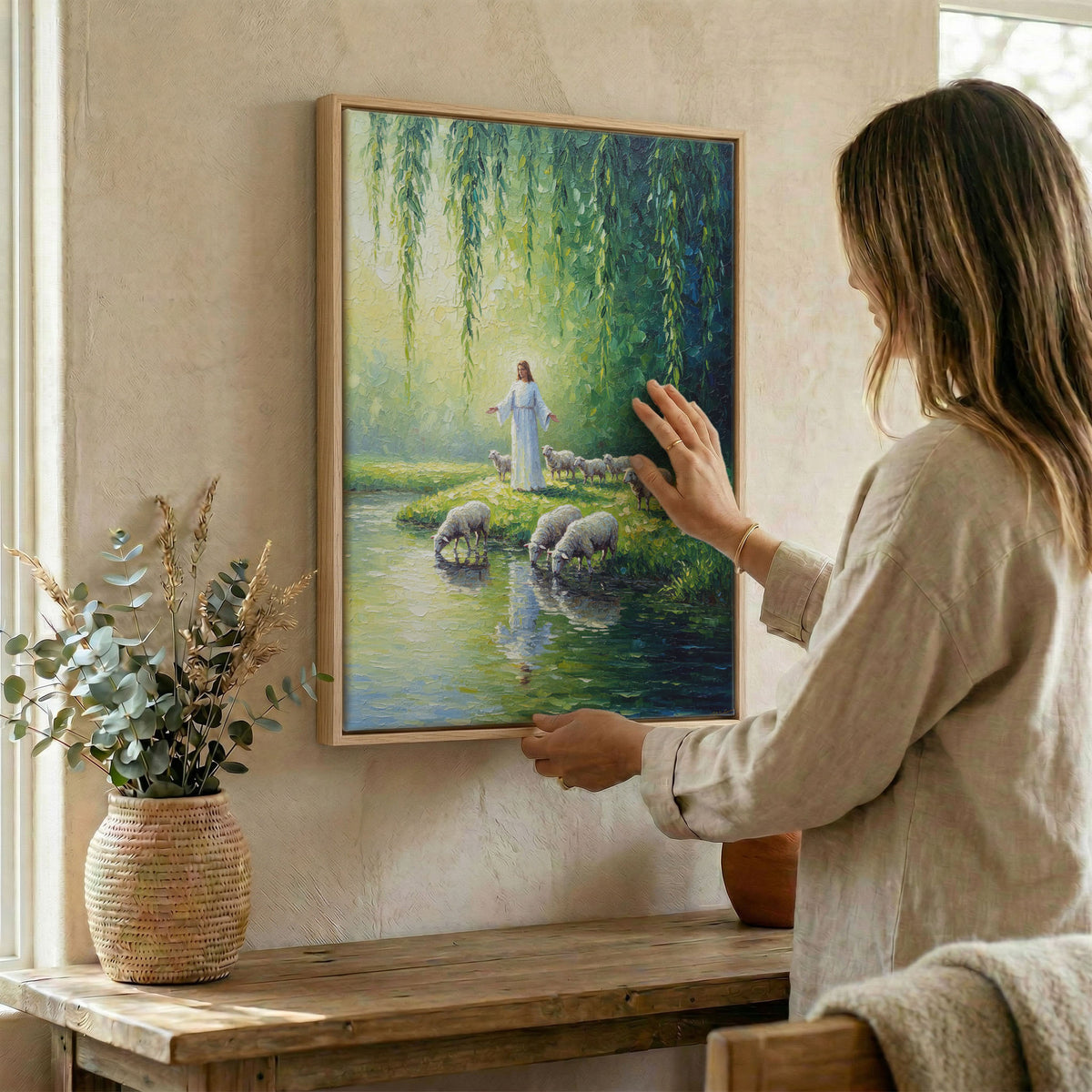 Woman hanging Jesus and sheep wall art in wood frame beside dried botanical arrangement