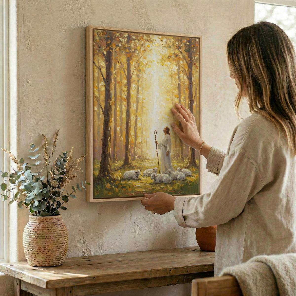 Woman hanging Jesus and sheep wall art in wood frame beside dried botanical arrangement
