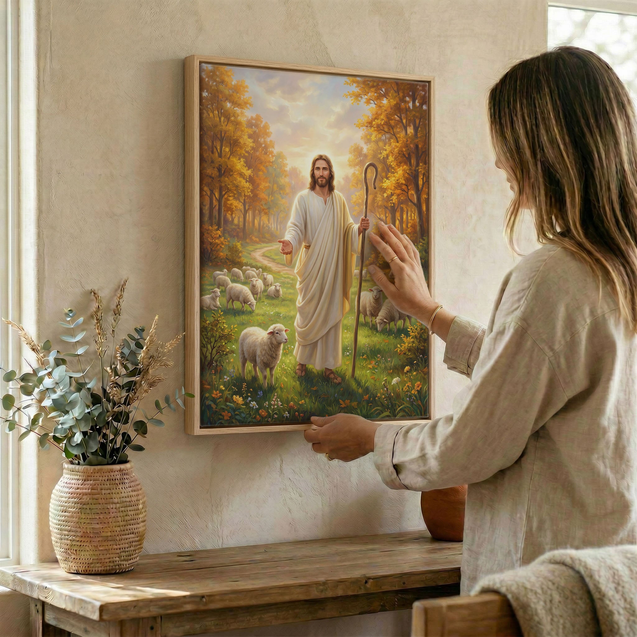 Woman hanging Jesus and sheep wall art in wood frame beside dried botanical arrangement