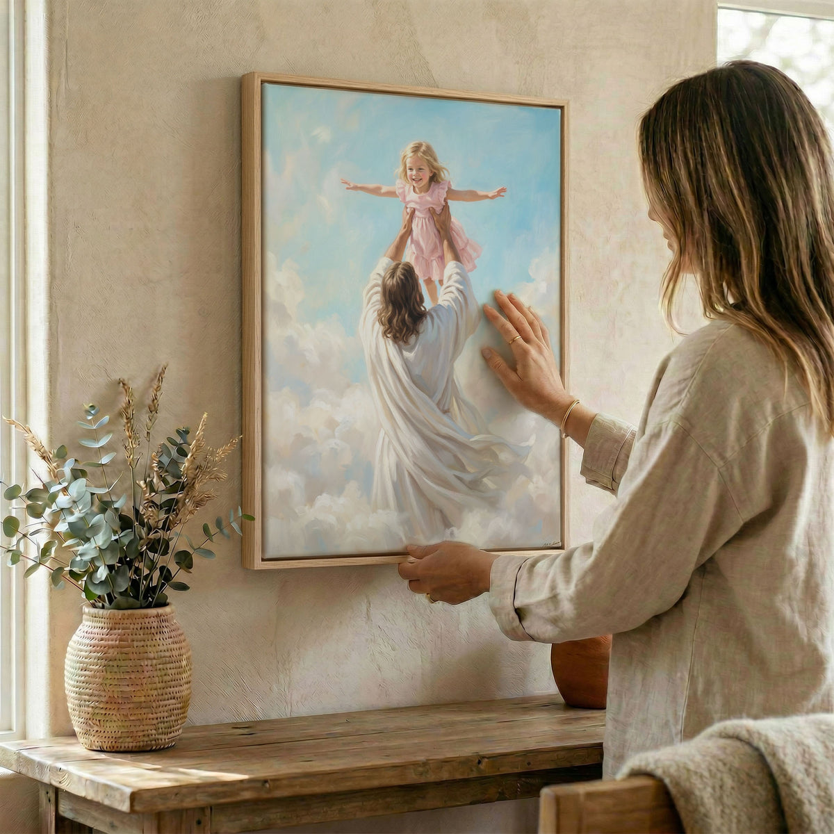 Woman hanging Jesus and child wall art in wood frame beside dried botanical arrangement