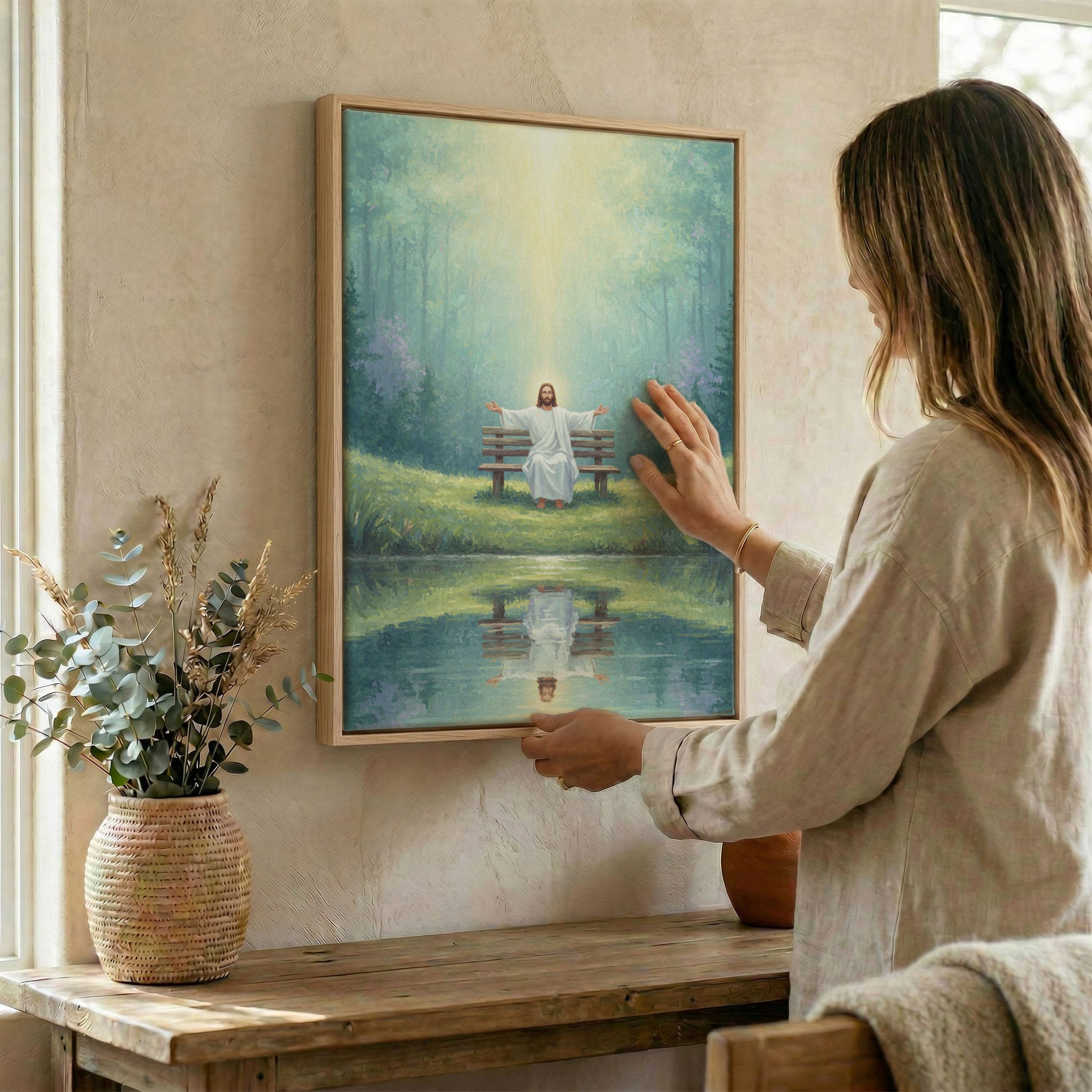 Woman hanging Jesus forest pond wall art in wood frame beside dried botanical arrangement