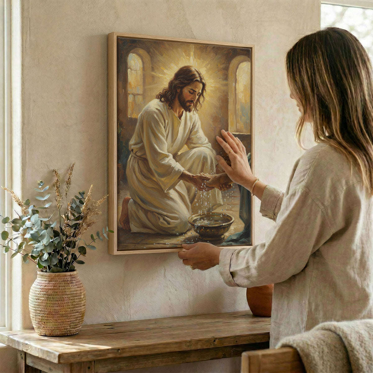 Woman hanging Jesus washing feet wall art in wood frame beside dried botanical arrangement