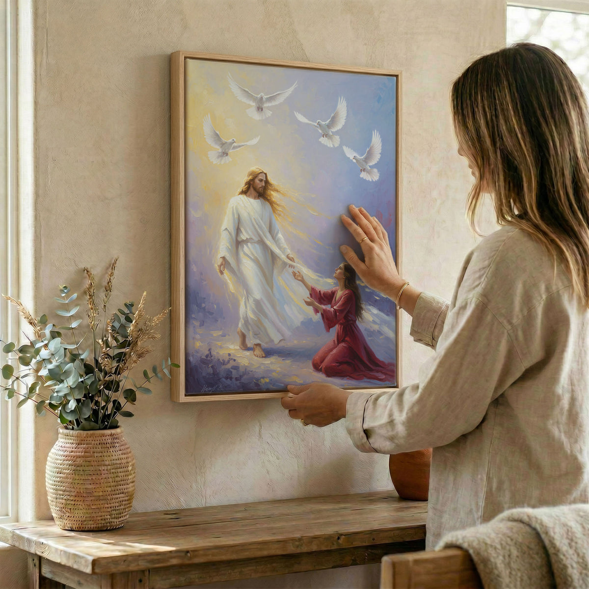 Woman hanging Jesus and woman wall art in wood frame beside dried botanical arrangement