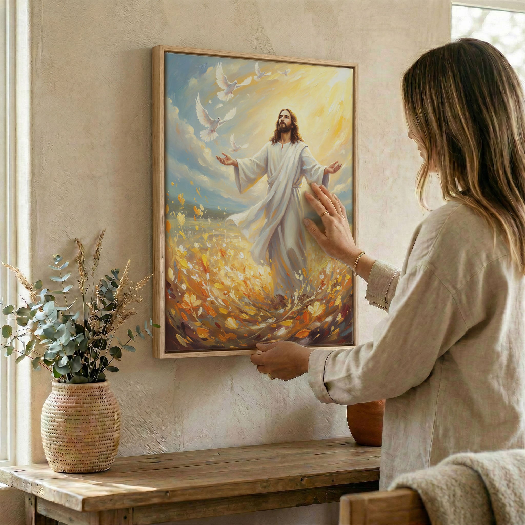 Woman hanging Jesus and doves wall art in wood frame beside dried botanical arrangement