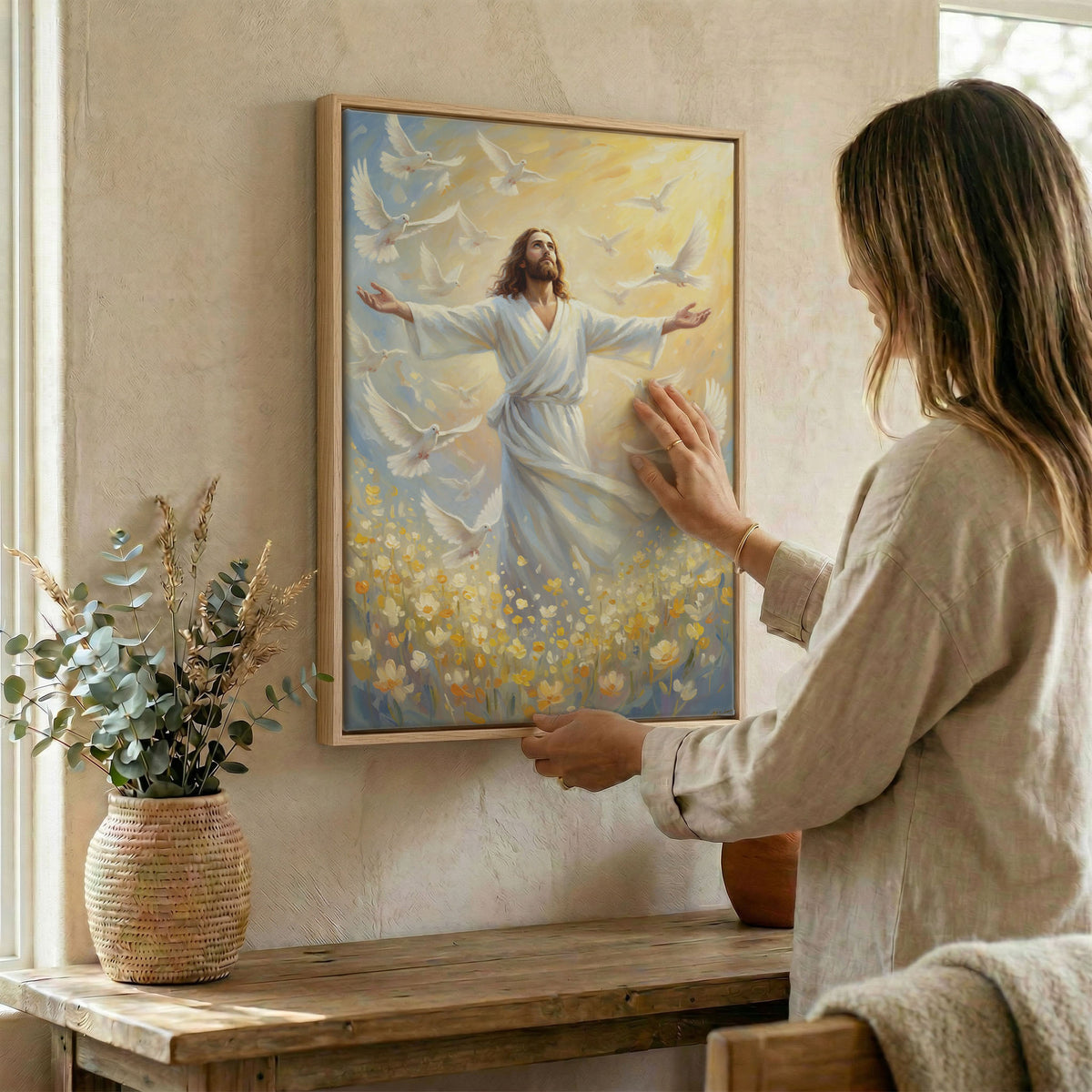 Woman hanging Jesus and doves wall art in wood frame beside dried botanical arrangement