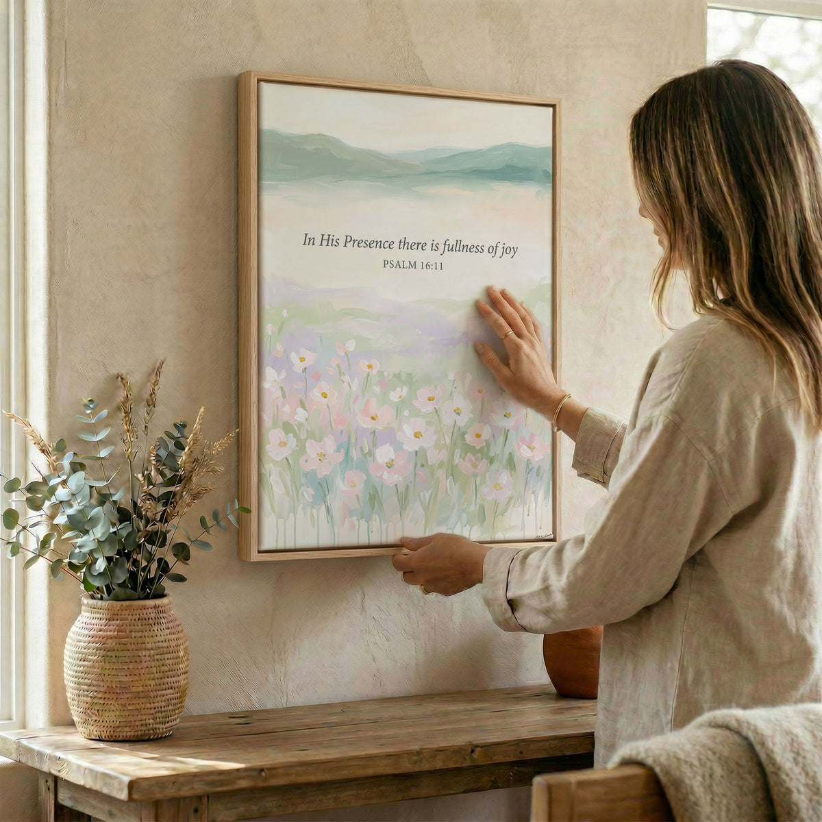 Woman hanging Psalm 16:11 floral wall art in wood frame beside dried botanical arrangement
