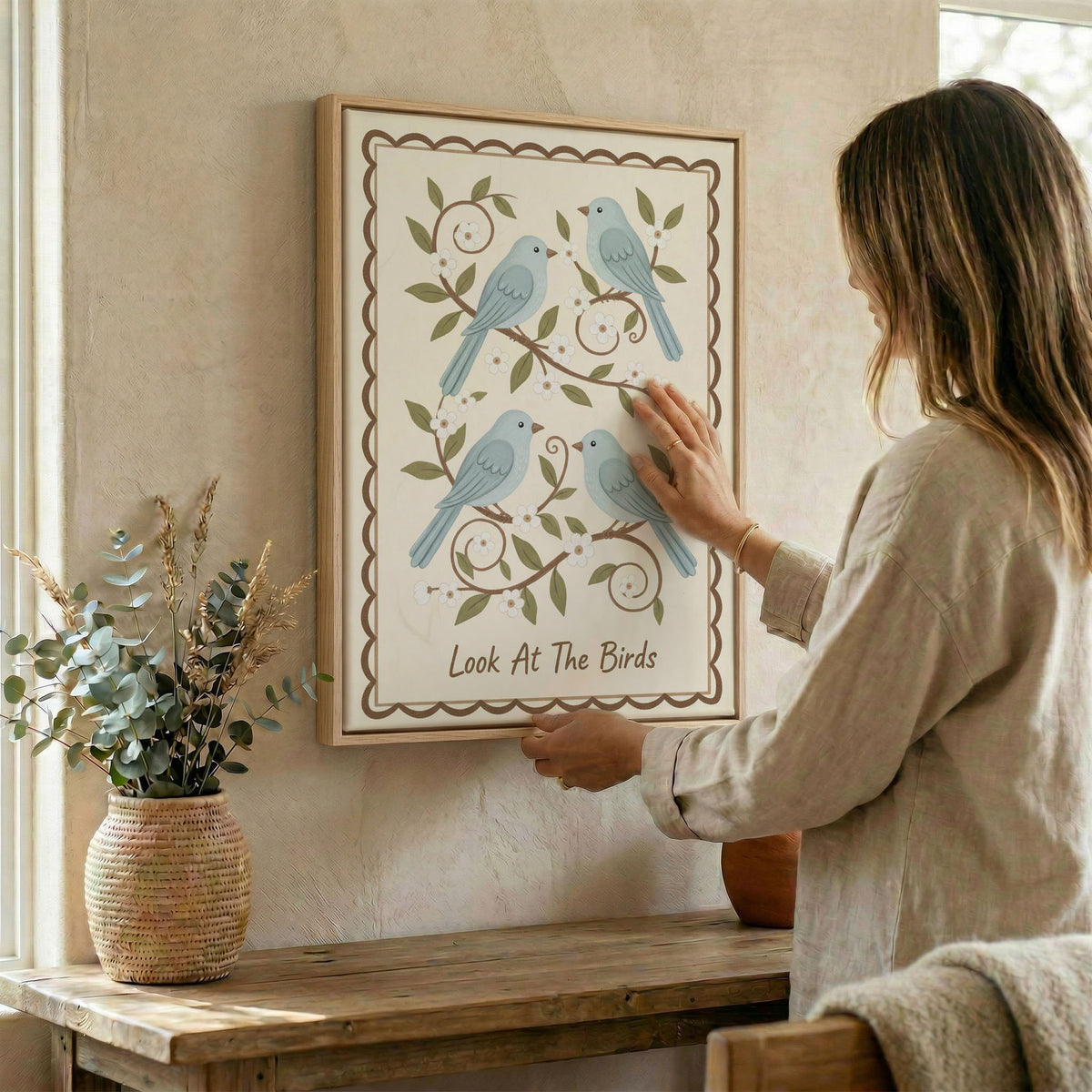 Woman hanging Look At The Birds canvas wall art with blue birds and floral vines in natural wood frame