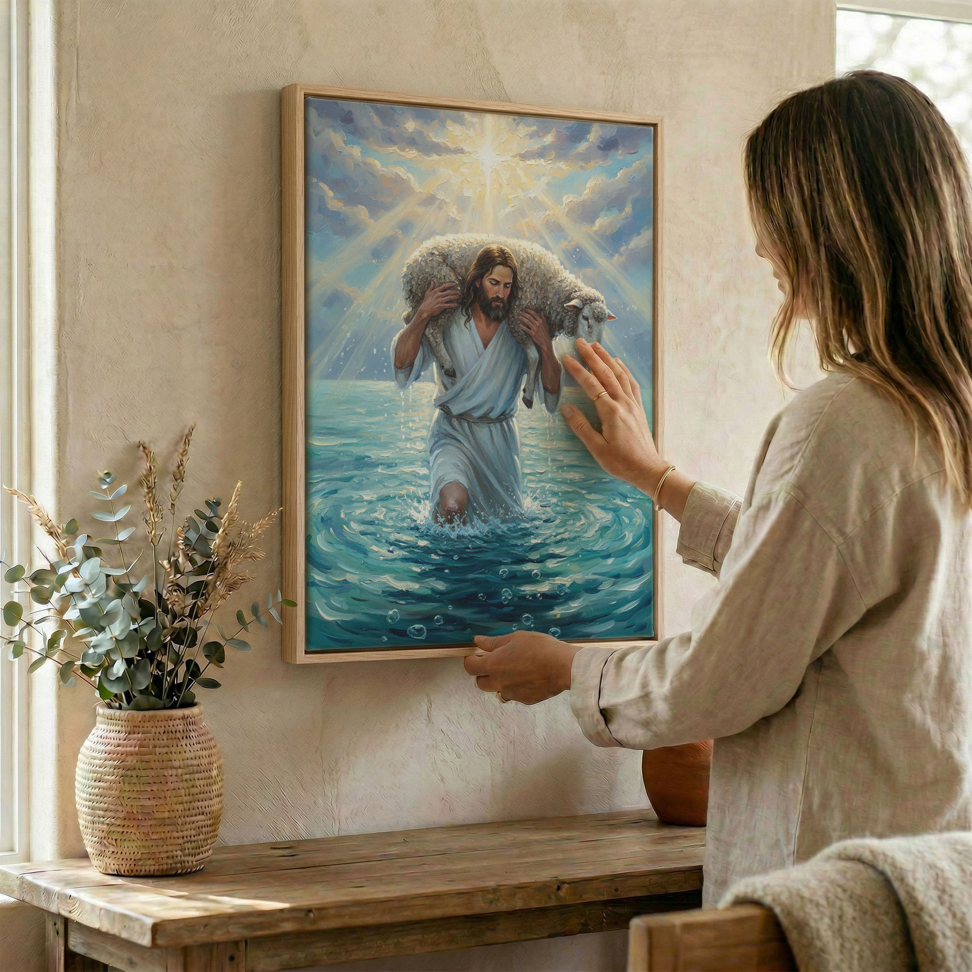 Woman hanging Jesus Good Shepherd and lamb wall art in wood frame beside dried botanical arrangement
