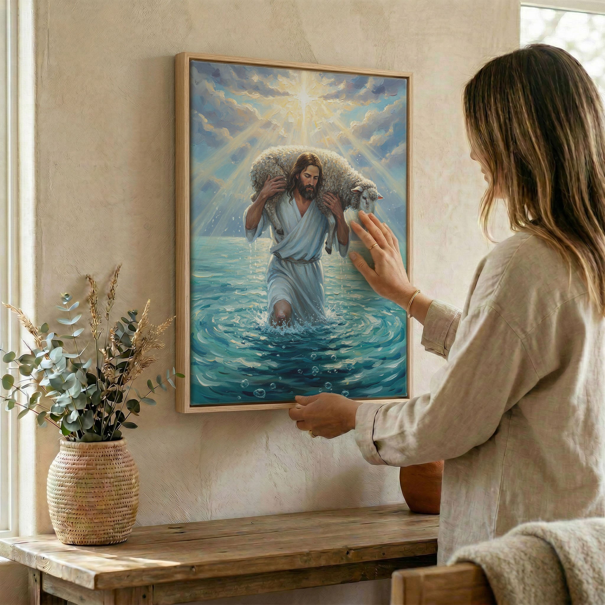 Woman hanging Jesus Good Shepherd and lamb wall art in wood frame beside dried botanical arrangement