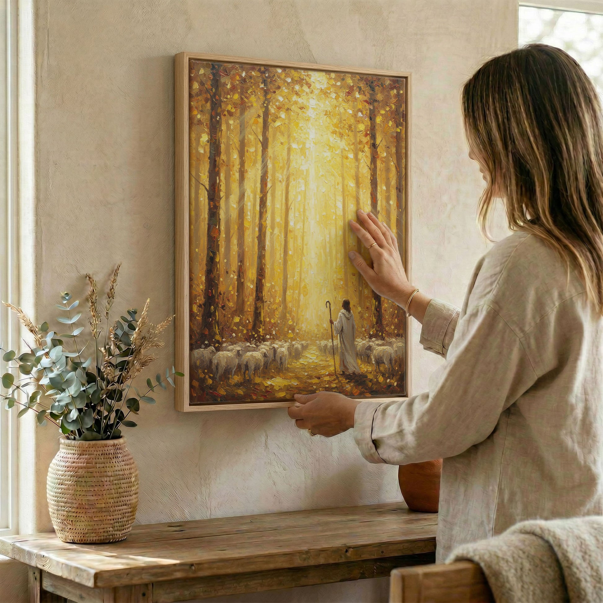 Woman hanging Jesus Good Shepherd autumn forest wall art in wood frame beside dried botanical arrangement