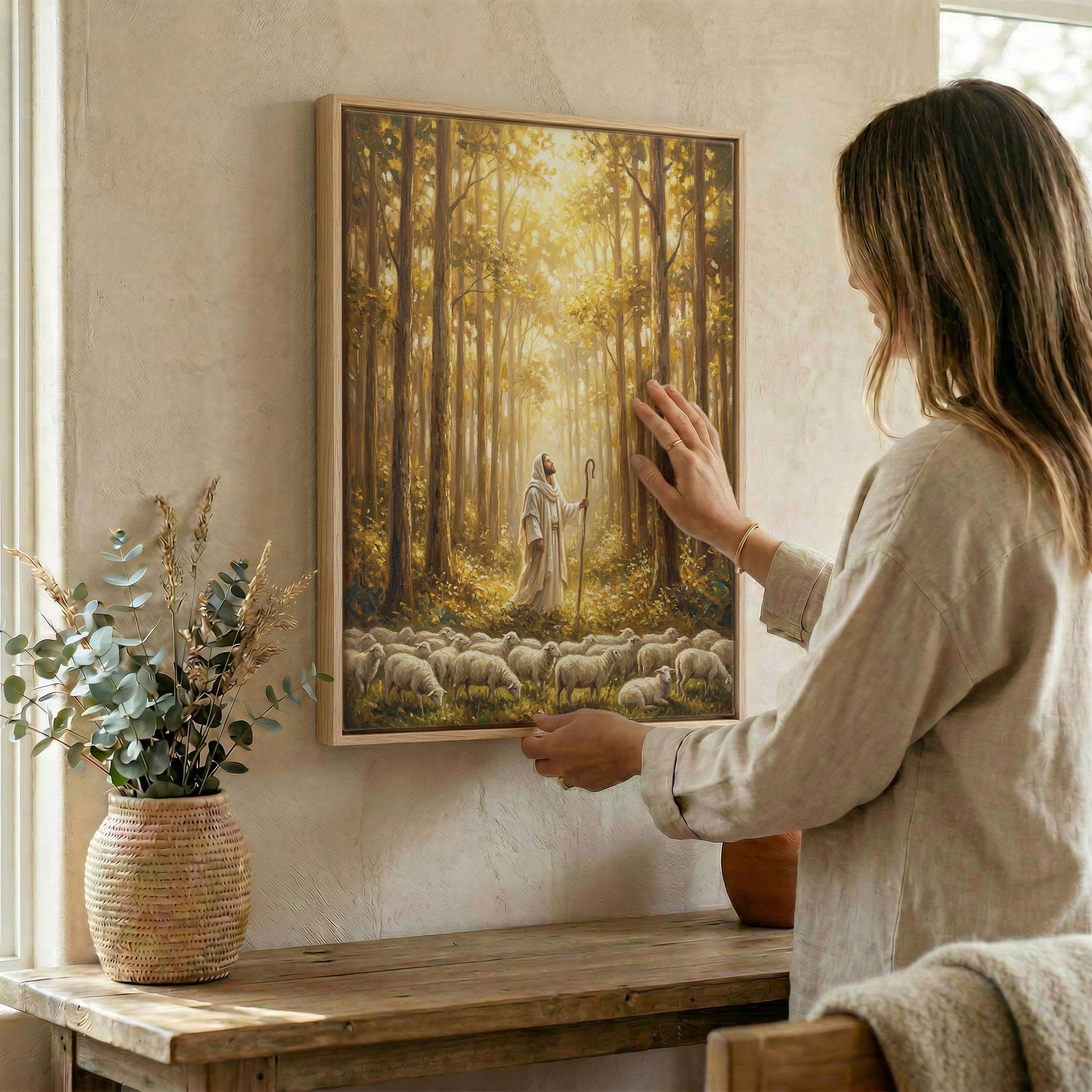 Woman hanging Jesus Good Shepherd forest wall art in wood frame beside dried botanical arrangement