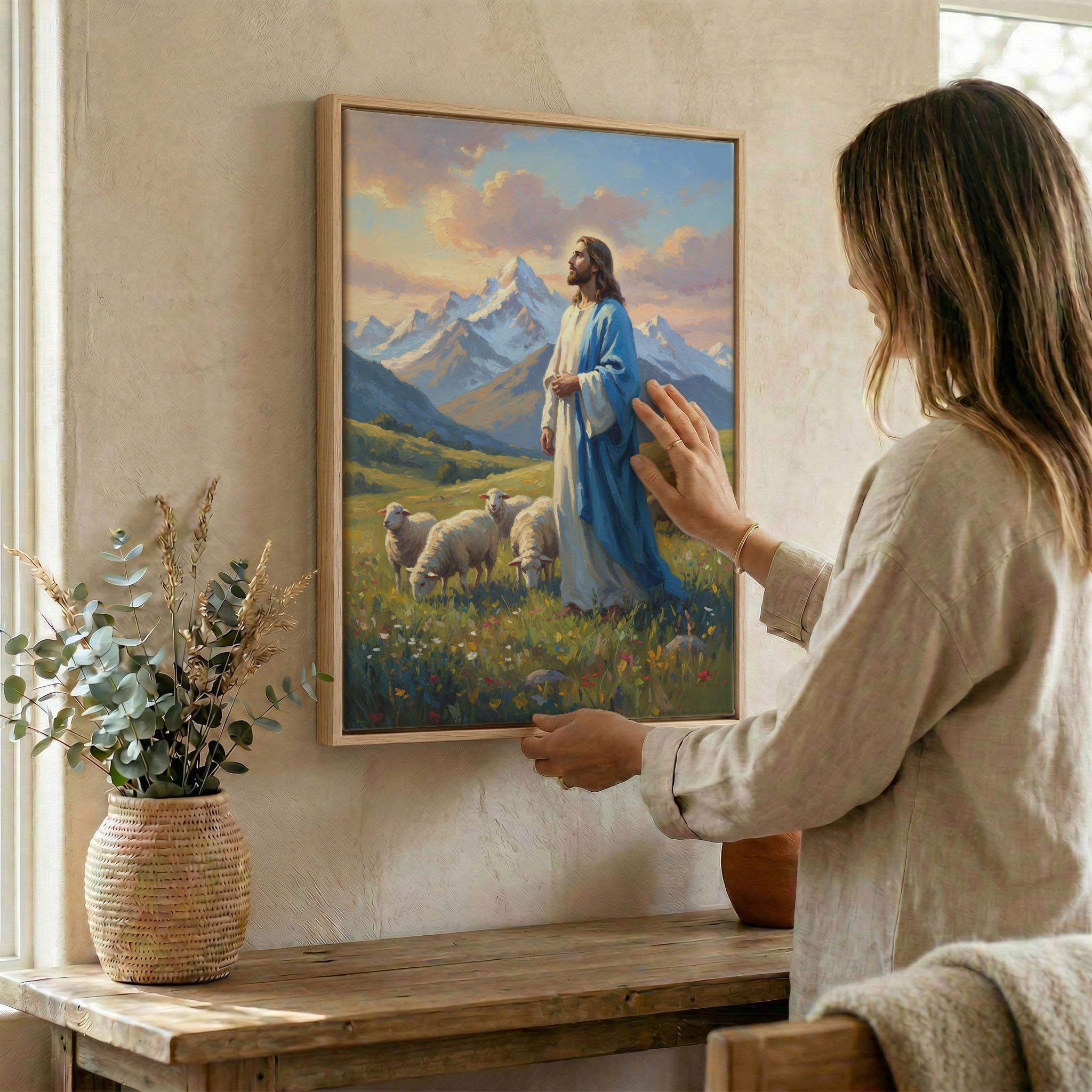Woman hanging Jesus Good Shepherd mountain wall art in wood frame beside dried botanical arrangement